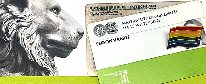 Symbolic image: Name change at MLU
[Image description: On the left half of the image you can see the head of the lion of the Lwengebude. In his direction of view, an identity card and a personal card of MLU are lying in the right half of the picture. The ID card photo is obscured by a rainbow pin].