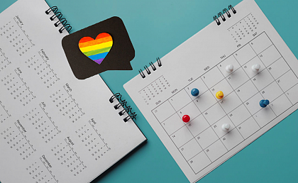 Symbolbild: LSBTIQ* Veranstaltungen
[Bildbeschreibungen: Auf trkisfarbenem Hintergrund liegen zwei Kalender. Auf der Monatsansicht sind mehrere Tage mit bunten Pins markiert. ber den Kalendern ist eine schwarze Sprechblase mit einem regenbogenfarbenen Herzen zu sehen.]